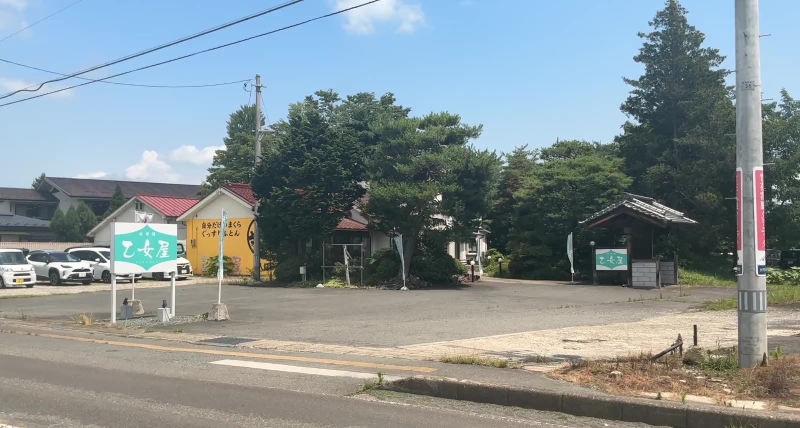 道路の向かいから見た乙女屋。ティールの看板と黄色い壁の建物